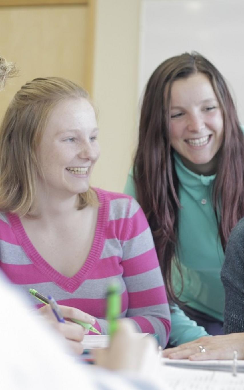 A teacher and students smiling together as they work